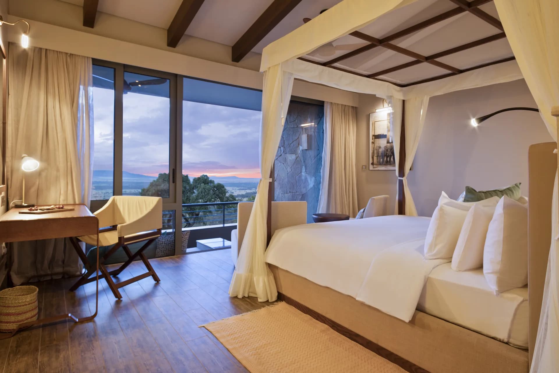 Panoramic room at Serengeti Lodge (Melia Collection), with a four-poster canopy bed and floor-to-ceiling windows overlooking the savanna at sunset
