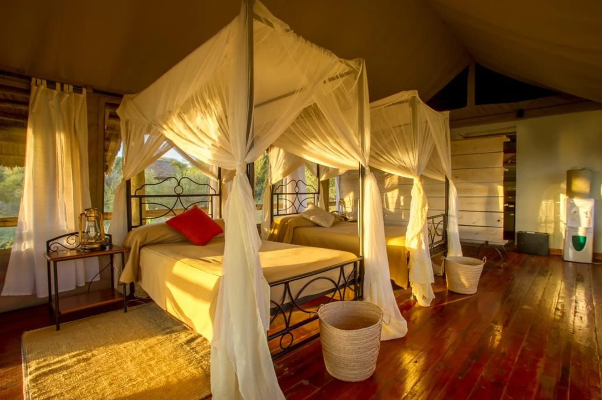 A multi-bed tented lodge room with three single beds under white mosquito netting, ideal for families traveling with children