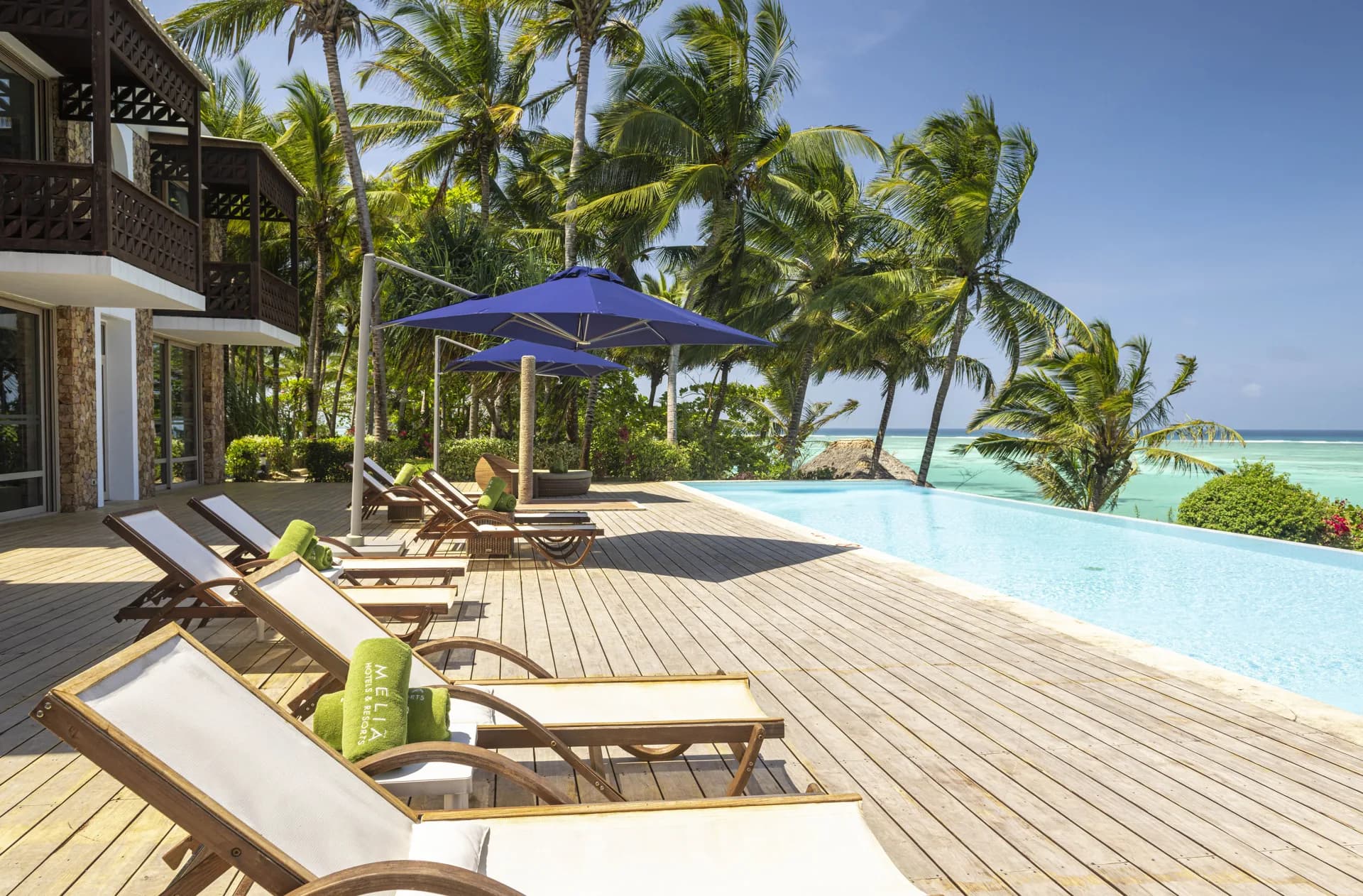 Infinity pool deck at Melia Zanzibar, lined with wooden loungers and palm trees overlooking the ocean