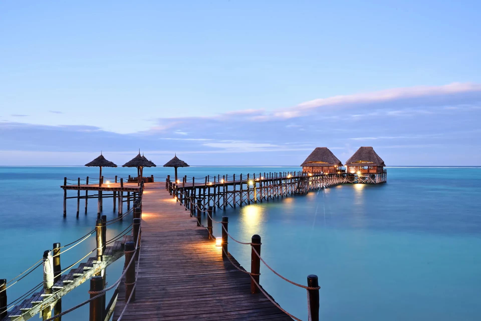 Lit wooden jetty extending into the water at a Zanzibar Melia resort at dusk